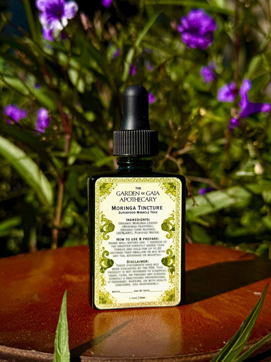 Bottle of Moringa Tincture with a dropper on a wooden surface with purple flowers in the background