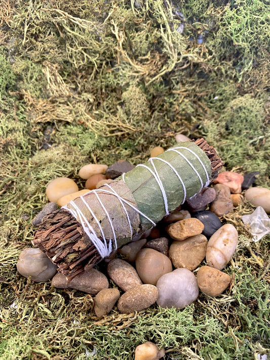 Lemon Balm & Peppermint Smudge Stick resting on pebbles and moss, showcasing its earthy texture and natural materials.
