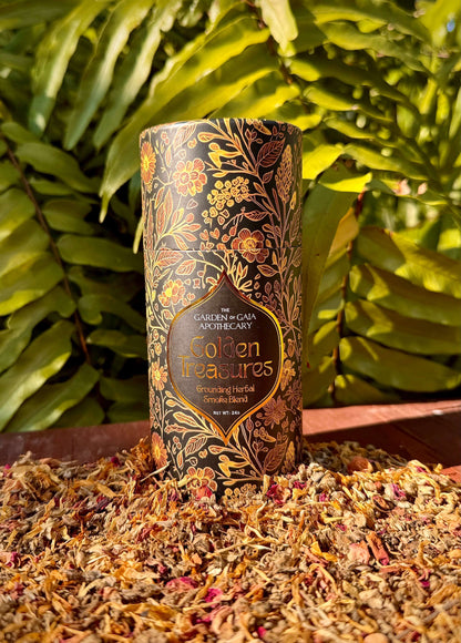 Golden Treasures-herbal smoke blend packaging surrounded by herbal materials and green foliage.