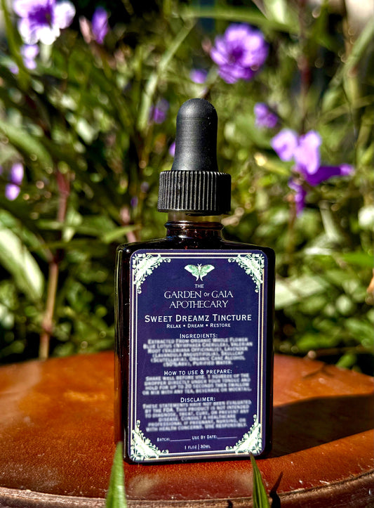 Bottle of Garden of Gaia Apothecary Sweet Dreamz Tincture with a dropper on a wooden surface with greenery in the background.