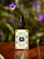 Blue Lotus Tincture bottle with dropper on a wooden surface with blurred purple flowers in the background