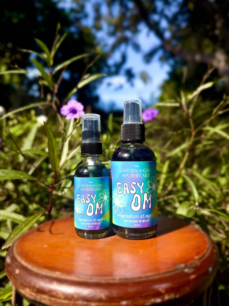 Two size bottles of 'Easy OM' product on a wooden surface with greenery in the background. 1 travel size and 1 large size.
