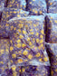 Stack of purple pillows with yellow floral patterns in clear plastic bags.